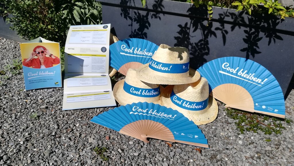 © Marina Fischer Fächer und Sonnenhüte mir der Aufschrift Cool bleiben liegen schön sortiert neben dem gleichnamigen Folder Cool bleiben