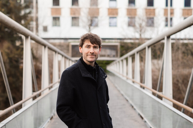 Manuel Pale Mann steht auf einer Brücke und lächelt.