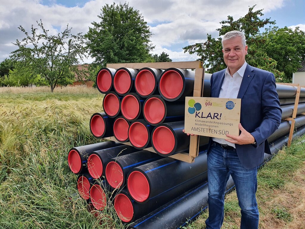 © GDA Foto im Freien vom Landtagsabgeordneten Anton Kasser (Obmann des GDA und Bürgermeister der e5-Gemeinde Allhartsberg) im Freien neben gestapelten Wasserrohren