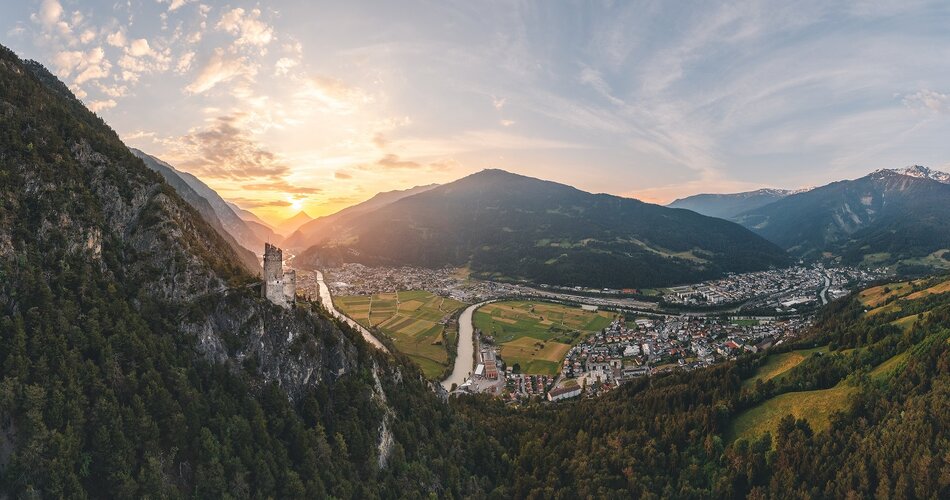 Roman Huber Im Sonnenuntergang sind Berge und einige Häuser und ein Fluss zu sehen.