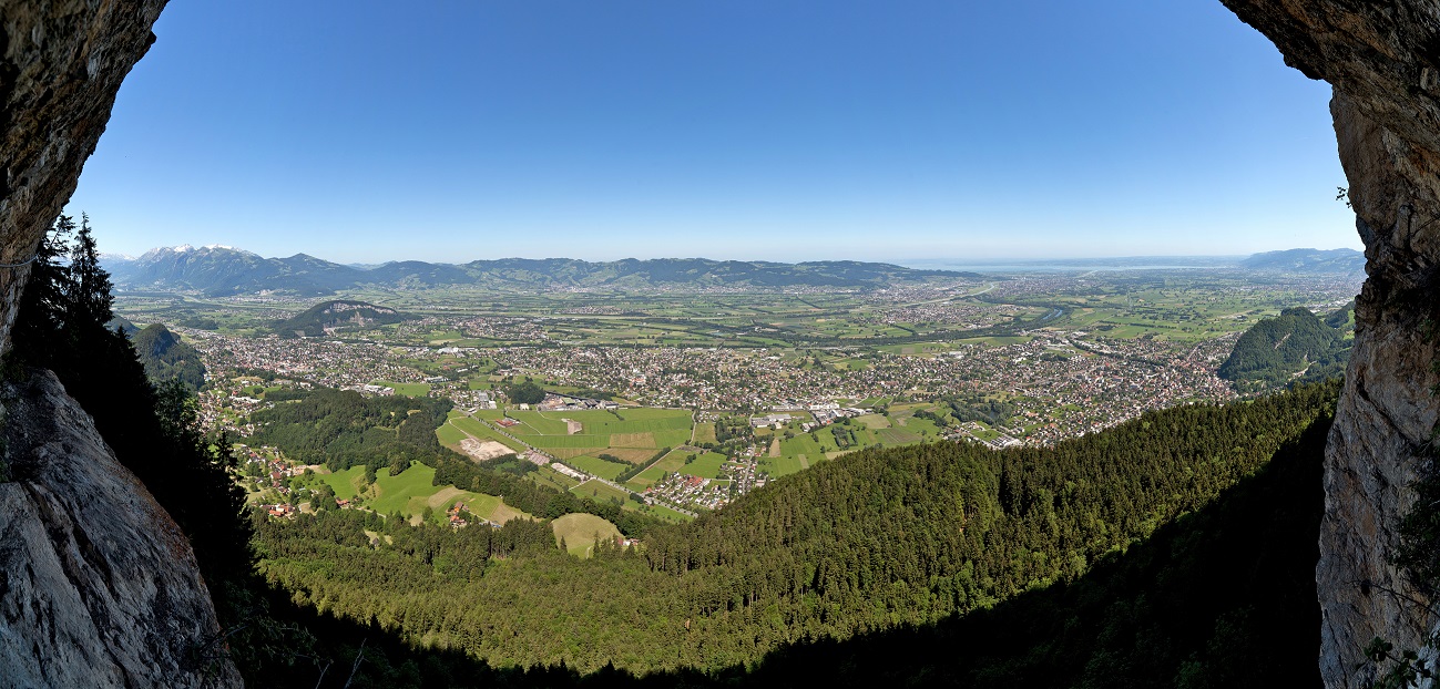 Links und rechts Felsen und in der Mitte Blick auf Häuser im Grünen mit Bergen im Hintergrund.