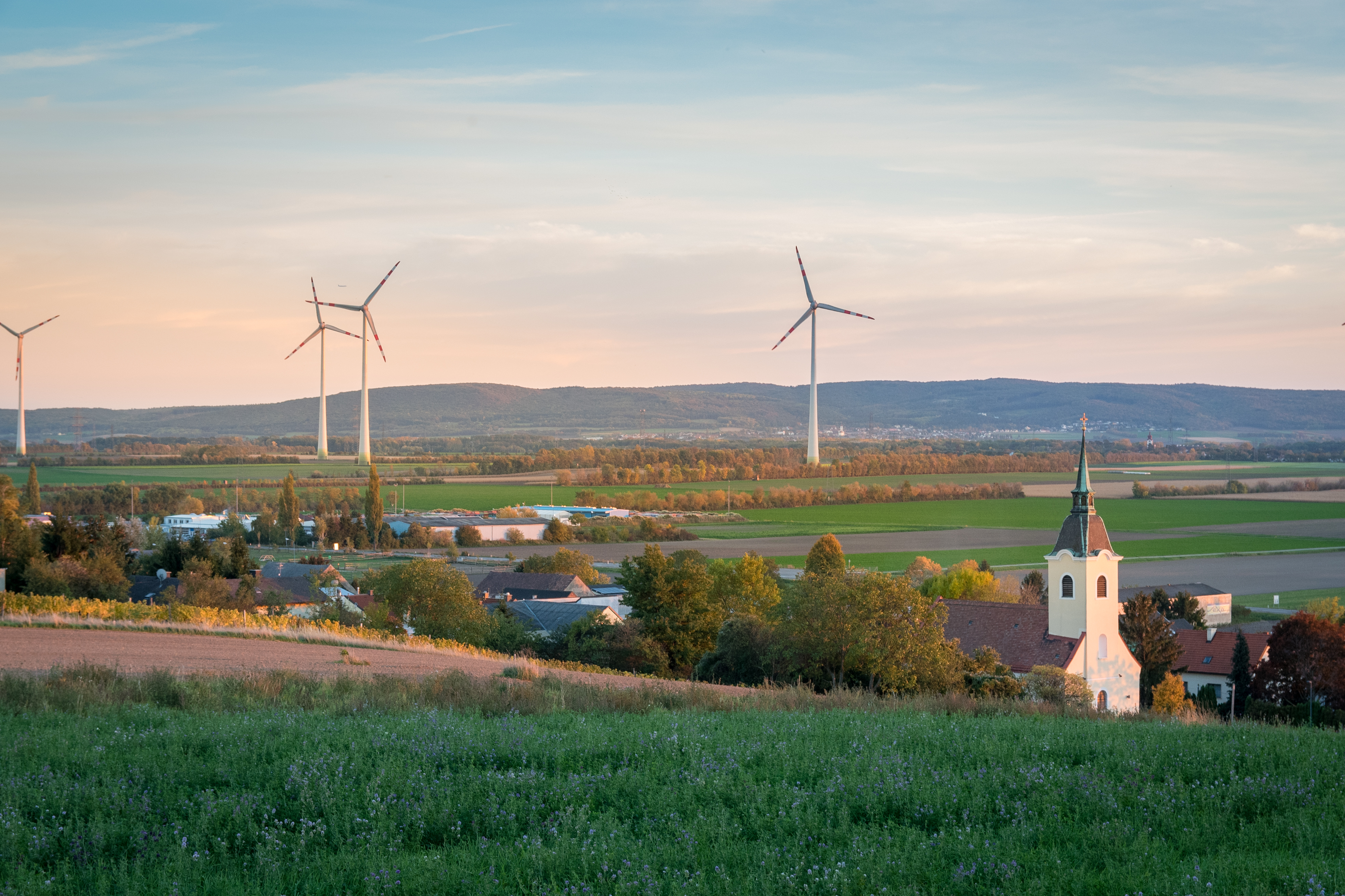 Kirche steht vorne rechts und links dahinter stehen Windräder. 