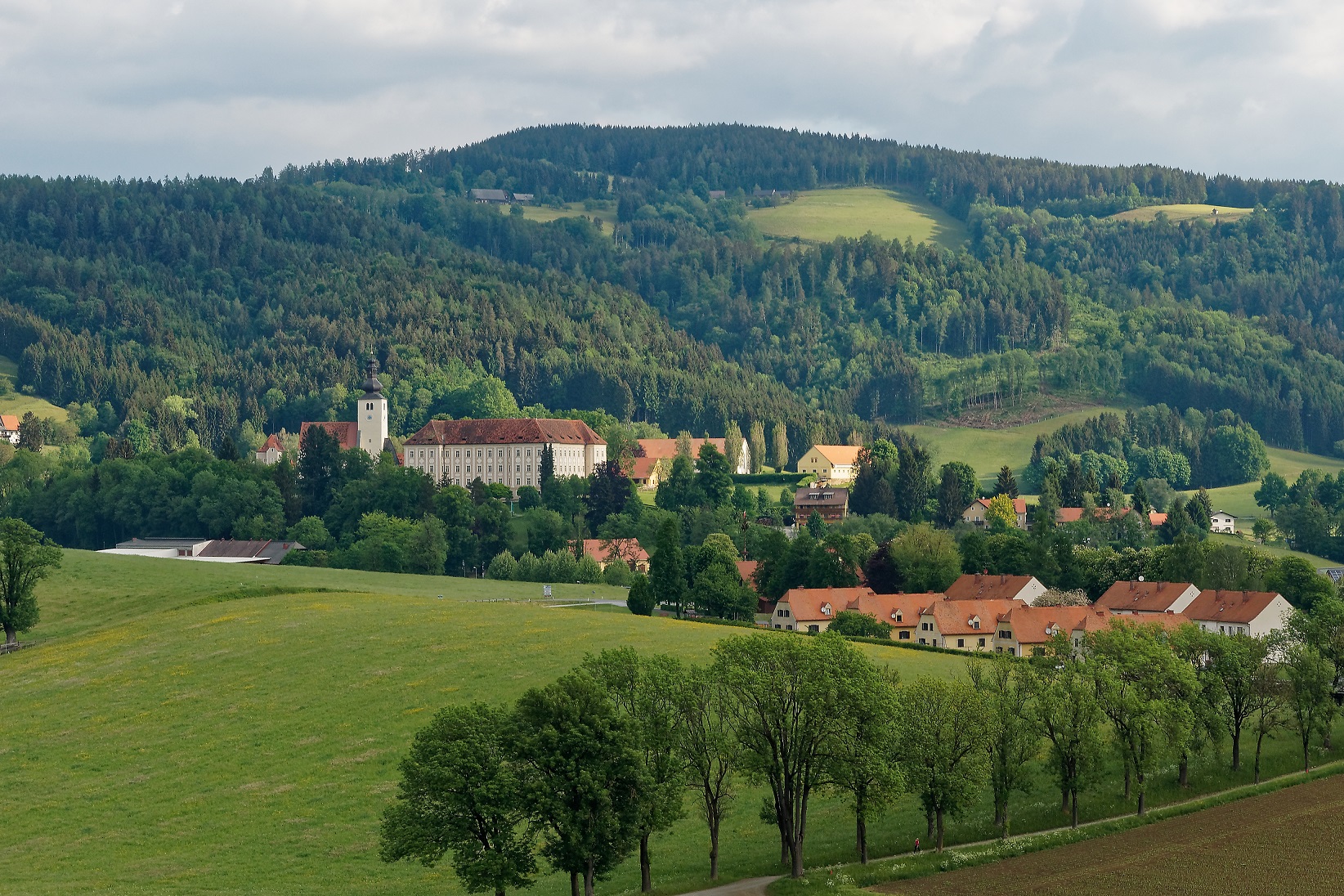 Landschaft mit Kirche und Siedlung von Köflach eingebettet in bewaldete Hügel